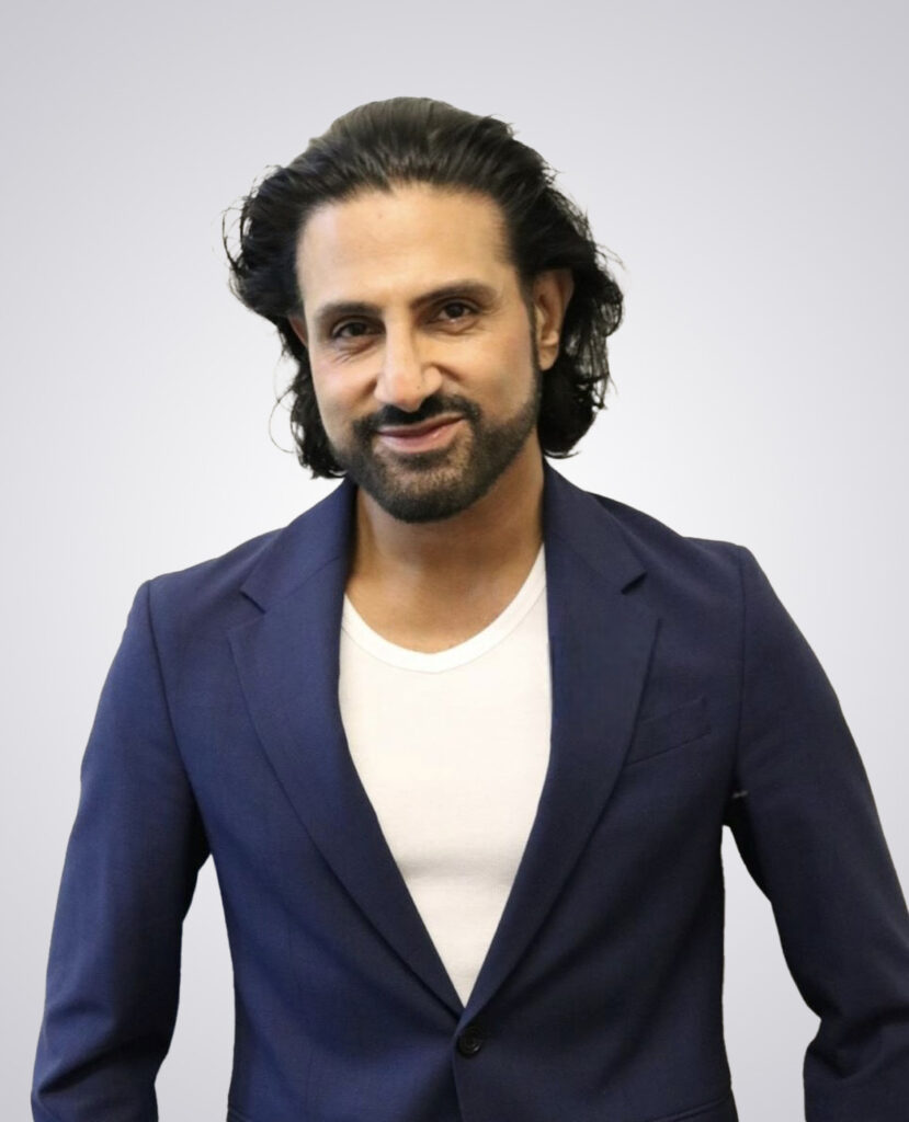 Professional headshot of a man with long black hair smiling wearing a navy blue blazer and white undershirt on a white background
