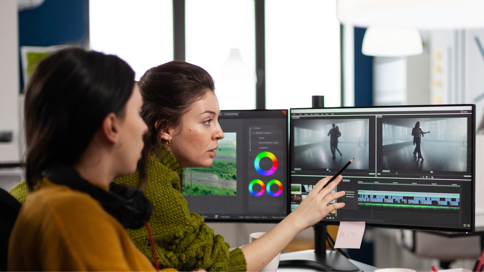 Two women looking at a computer monitor with post production software open with one women pointing with a pencil in her right hand to the screen