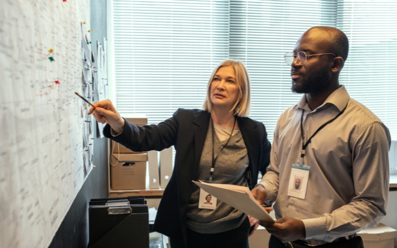 Woman pointing at a whiteboard while her male co-worker looks at the board