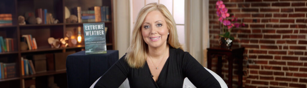 Blonde woman smiling in a black sweater sitting in a white chair in front of a brick wall
