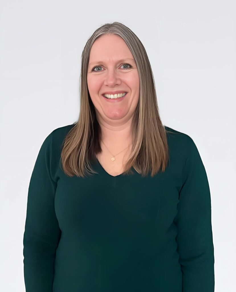 Professional headshot of a smiling woman in a green sweater - Vicki Hiney