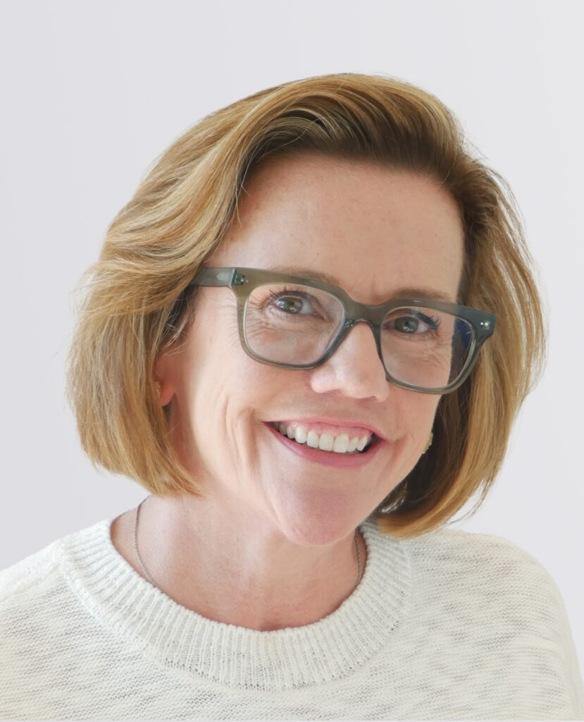 Professional headshot of a smiling woman with glasses in a white sweater.