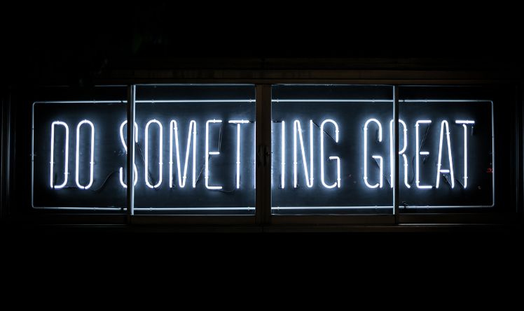 The text "do something great" capitalized made by a white neon sign on a black background