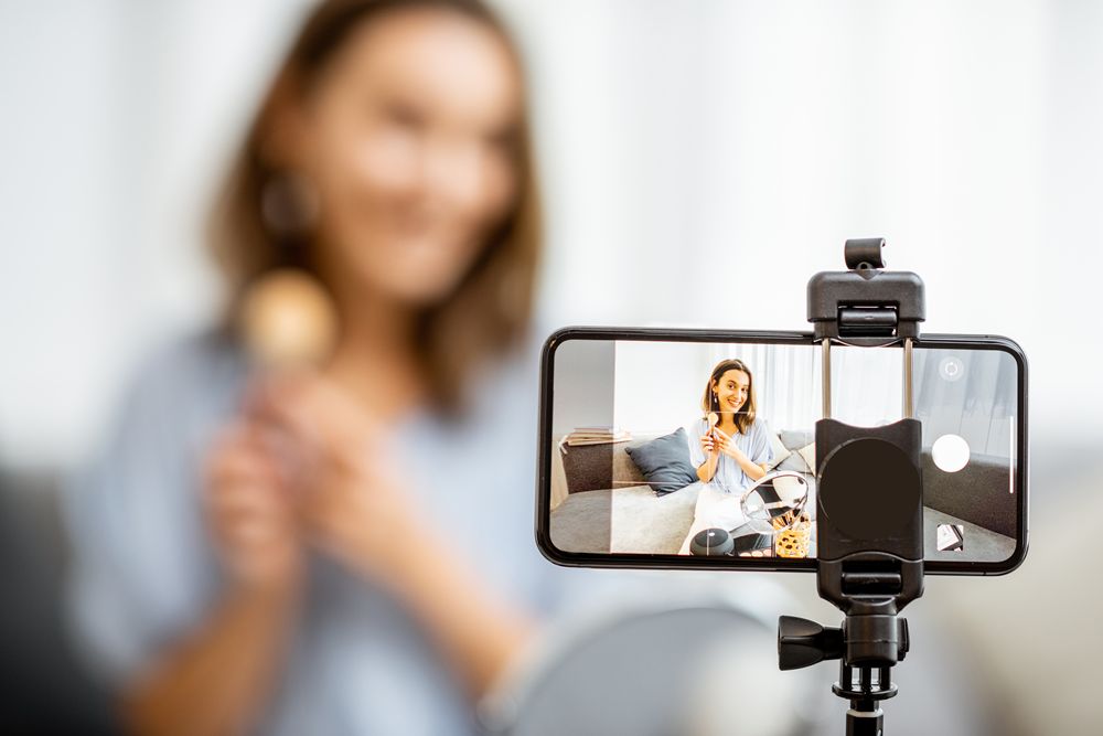Young woman recording on a smart phone her vlog about cosmetics, showing and demonstrating makeup, close-up on phone. Concept for influencer marketing strategy